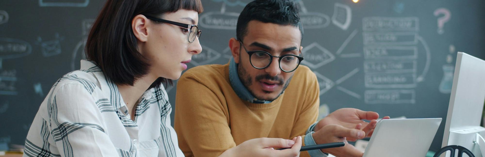 Photograph of a two people leaning over a laptop and discussing what they see on the screen.