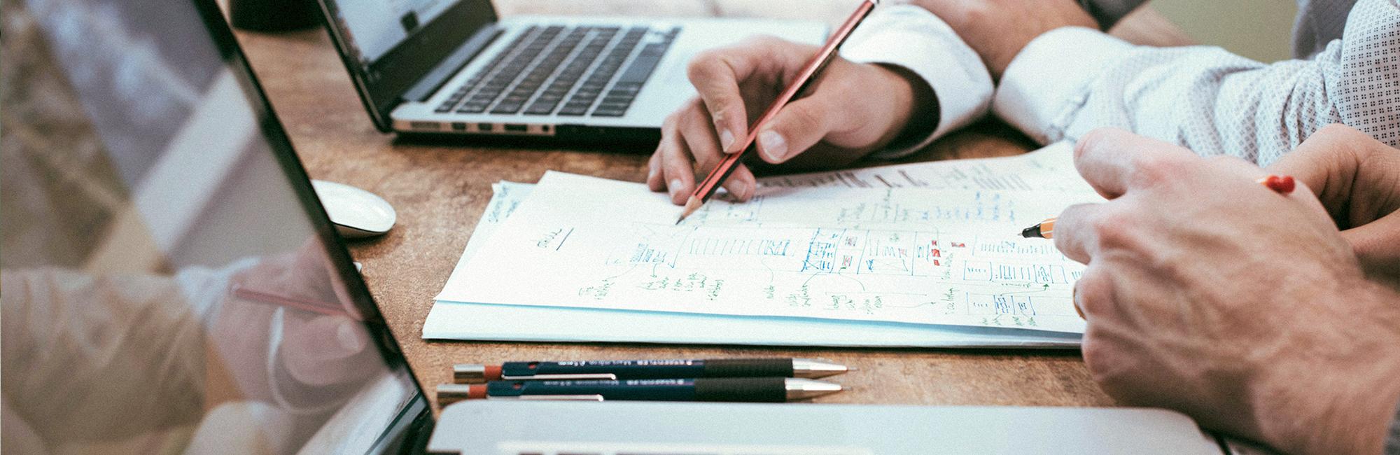 Photograph of a group of people in front of a computer, taking notes and drawing a diagramon a piece of paper.