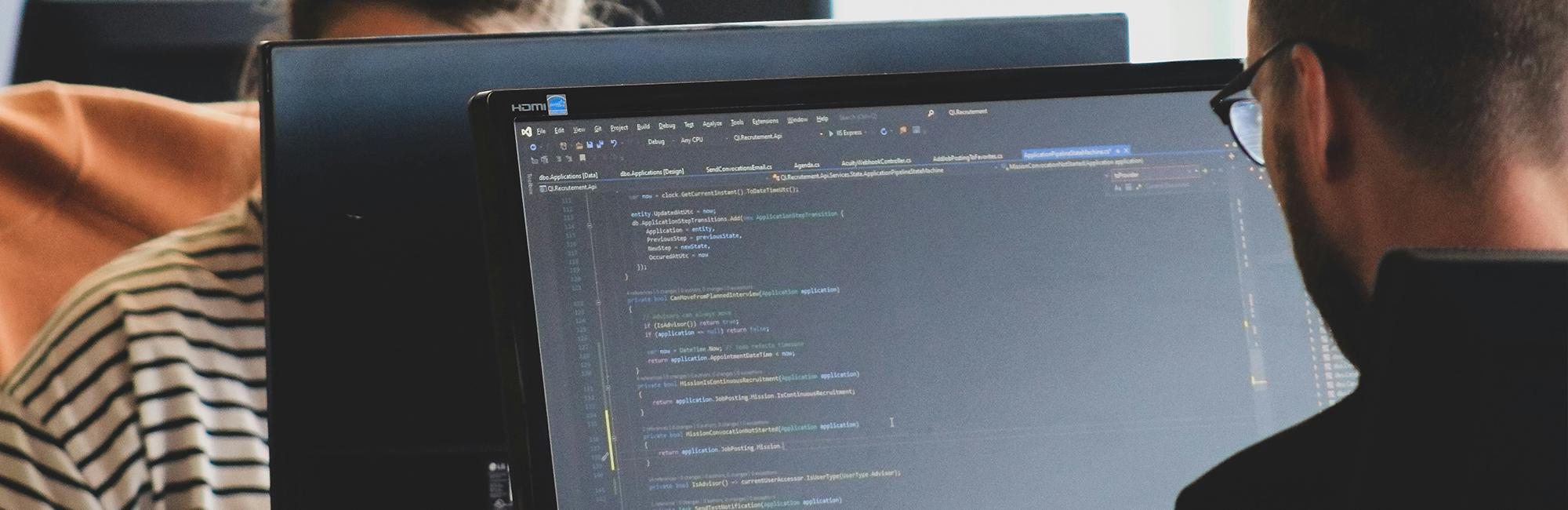 Photograph of a man in front of a computer, writing code.